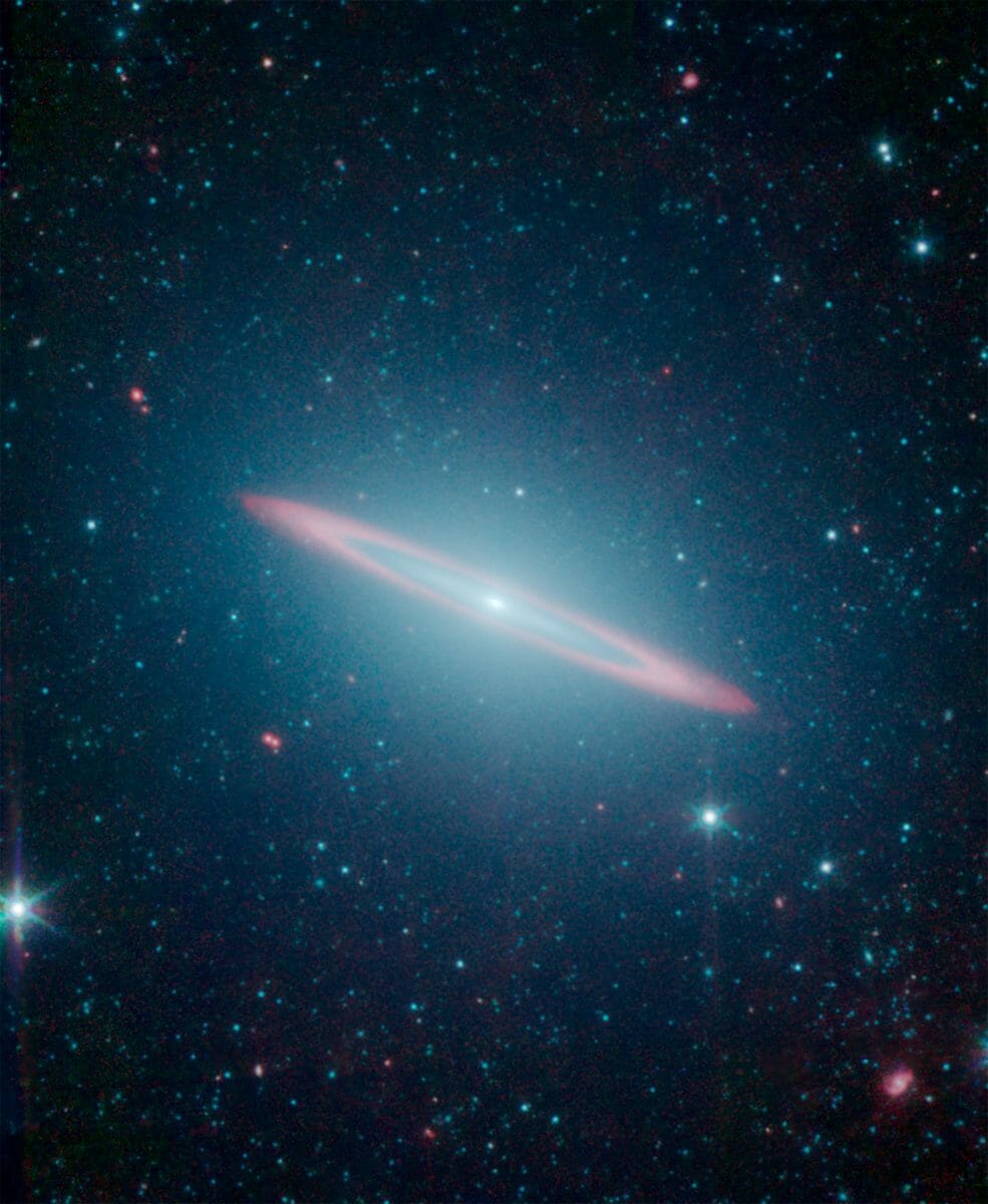 【▲ スピッツァーによって撮影されたソンブレロ銀河（疑似カラー）。楕円銀河（淡く広がる青）のなかに渦巻銀河の円盤（赤）が埋め込まれたような構造をしている（Credit: NASA/JPL-Caltech）】