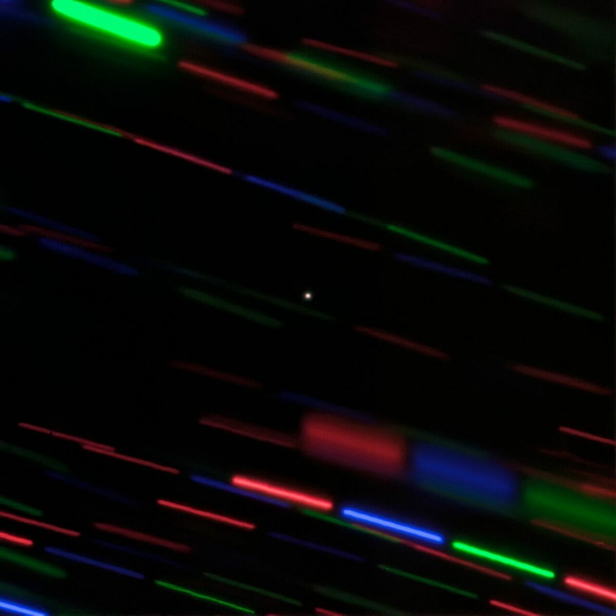 ハワイ・マウナケア山の「ジェミニ北望遠鏡」が撮影した「2020 CD3」（中央）。高速で移動する2020 CD3の動きに合わせて望遠鏡を動かしつつ三色のフィルターを切り替えながら撮影したため、背景の星々はカラフルな点線として写っている