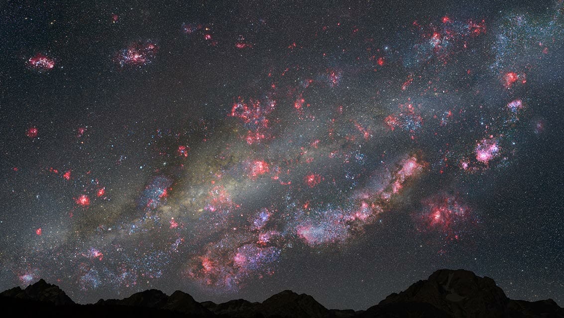 100億年前の天の川銀河のような、若い銀河の中にある仮想の惑星から見た夜空の想像図。ピンク色のガス雲の中には生まれたばかりの星があり、青白い若い星団が夜空に散らばっています。（Credit：NASA / ESA / Z。Levay（STScI））