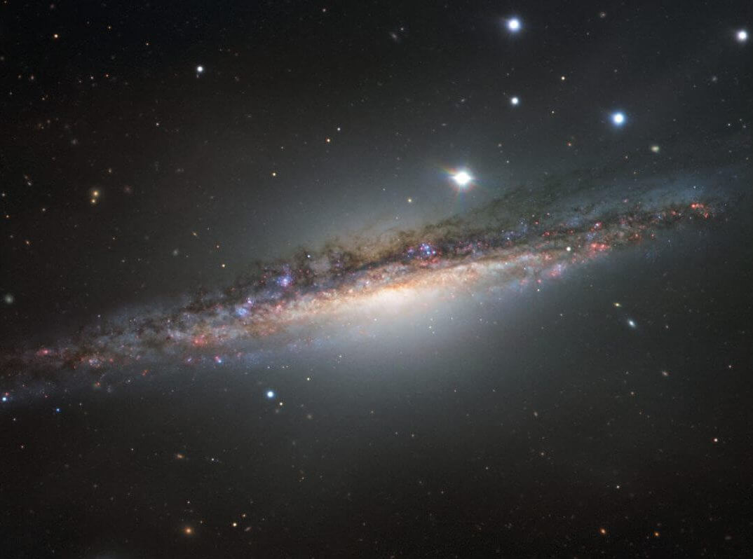 相互作用で波打つ渦巻銀河、超大型望遠鏡が捉えた“くじら座”の「NGC 1055」