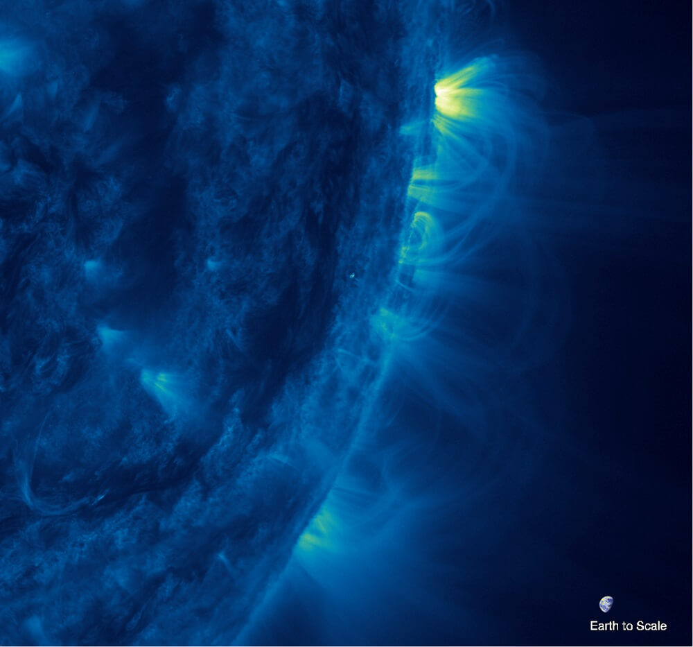 【▲NASAの太陽観測衛星SDOに搭載されたAIA機器によって335Å（＝33.5nm）の波長で撮影された太陽のコロナループ。この画像では、ループは高さ方向にあまり広がらず、太陽表面から遠くまで伸びている。なお、右下に地球が縮尺表示されている（Credit: NASA/SDO）】