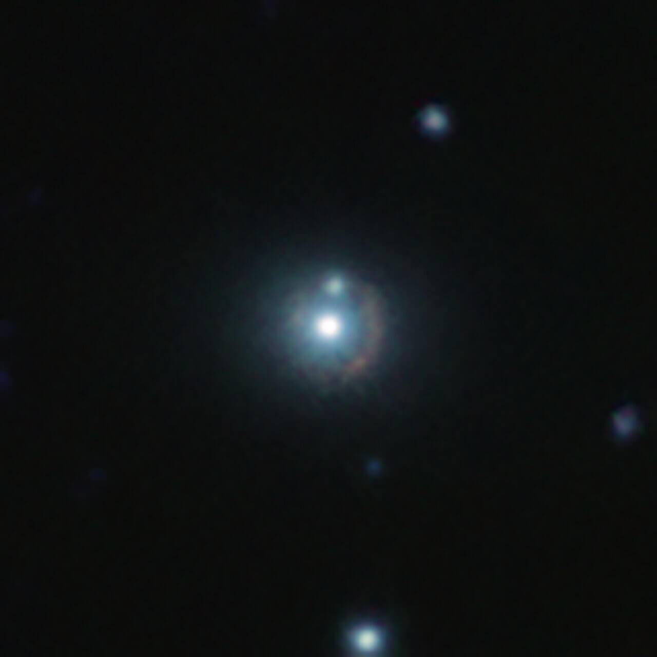 【▲ 図2: 9io9の赤外線画像。VISTA望遠鏡とカナダ・フランス・ハワイ望遠鏡の撮影画像を組み合わせたもの。中心部で光っているのは重力レンズ効果の重力源となっている別の銀河であり、その周りを囲む赤い孤が9io9の像である。 (Image Credit: ESO, J. Geach et al.) 】