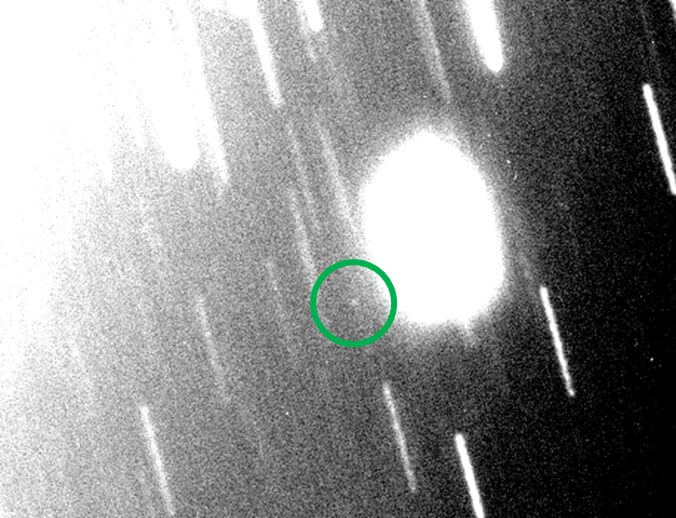 【▲図3: マゼラン望遠鏡で2023年11月4日に撮影されたS/2023 U 1 (丸囲み内部の白点) 。天王星は左上にあり、その一部が写り込んでいます。細長く伸びた線は背景にある恒星で、望遠鏡を天王星や衛星の動きに合わせて動かしたために相対的に動いた結果です。 (Image Credit: Scott S. Sheppard, Magellan telescope (丸囲みは筆者による加筆) 】