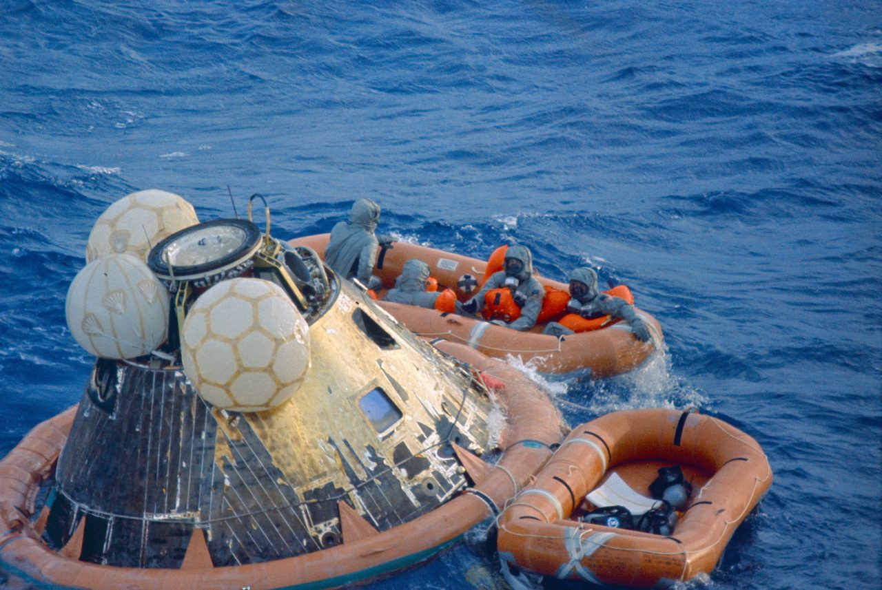 【▲ 司令船の着水後、アメリカ海軍士官とともにボートに乗り移ったアポロ11号の3名の宇宙飛行士。全員が隔離服を身に着けている（Credit: NASA）】