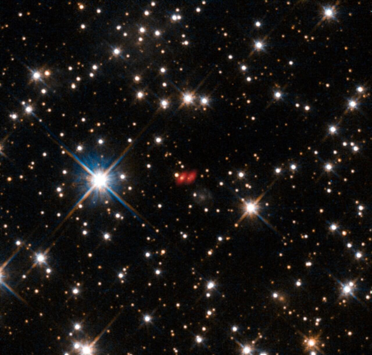 約74億年前の宇宙は今より2.4℃暑かった 高精度な温度測定でビッグバン宇宙論を検証 3 図3: ALMA望遠鏡によって撮影されたPKS 1830-211の疑似カラー画像(中央の赤い像)。ハッブル宇宙望遠鏡で撮影された背景の星空に重ねられています。重力レンズ効果によって像が2つに分裂しています。(Credit: ALMA(ESO, NAOJ & NRAO), NASA , ESA & I. Martí-Vidal)