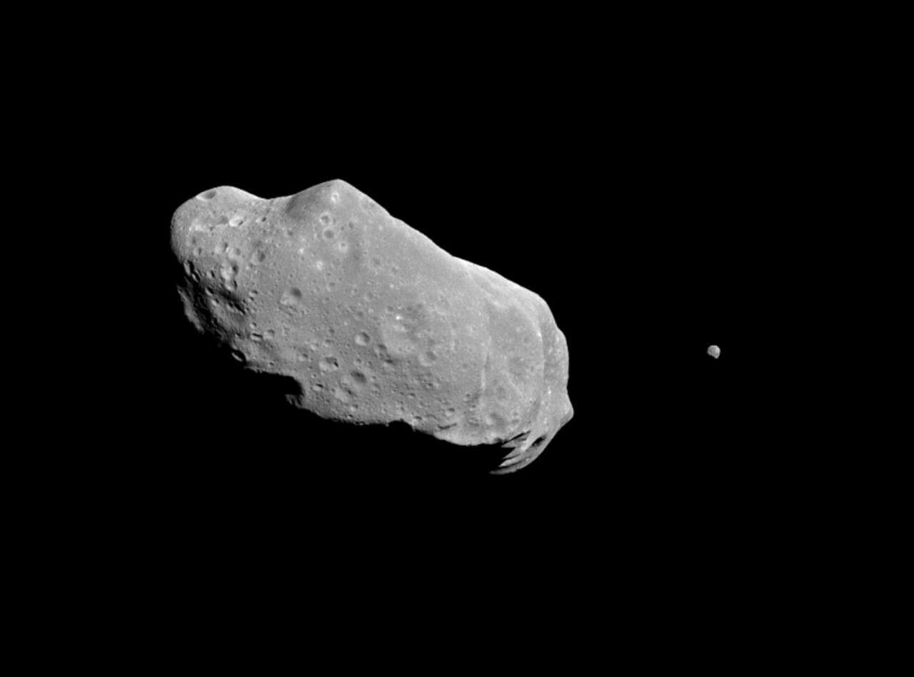 木星探査機ガリレオが撮影した小惑星イダとその衛星ダクティルの画像。画面左側に細長い小惑星イダが横向きに写り、クレーターだらけの表面が見える。右側の離れた位置には、小さな点のようにイダを回る衛星ダクティルが映っている