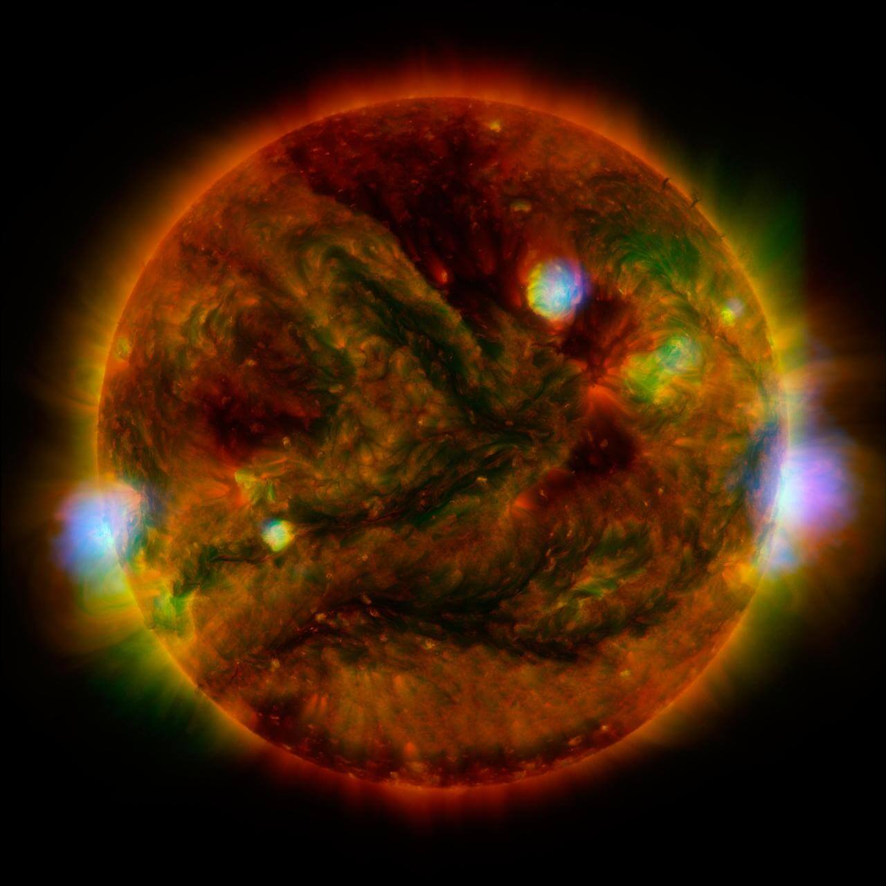 図1：太陽は、電波からX線まで広範な波長の電磁波を放出しています。その中心となる波長は可視光のオレンジから青の領域であり、太陽の表面温度5500℃（5800K）を反映しています。映像は、NASAの太陽観測衛星「ソーラー・ダイナミクス・オブザーベトリー（SDO）」と宇宙望遠鏡「NuSTAR」、それにJAXAの「ひので」がとらえた極短紫外線（赤、黄）およびX線（緑、青）のデータにもとづく太陽の姿。(Credit: NASA/JPL-Caltech/GSFC/JAXA)